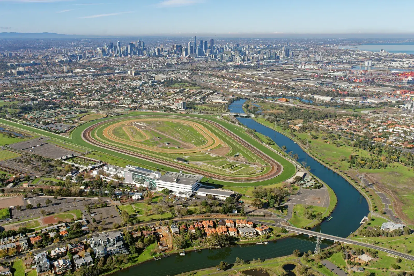 สนามแข่งม้า Flemington มองจากมุมสูง มีแม่น้ำ Maribyrnong โค้งรอบสนาม และตึกในเมืองเมลเบิร์นอยู่ด้านหลัง