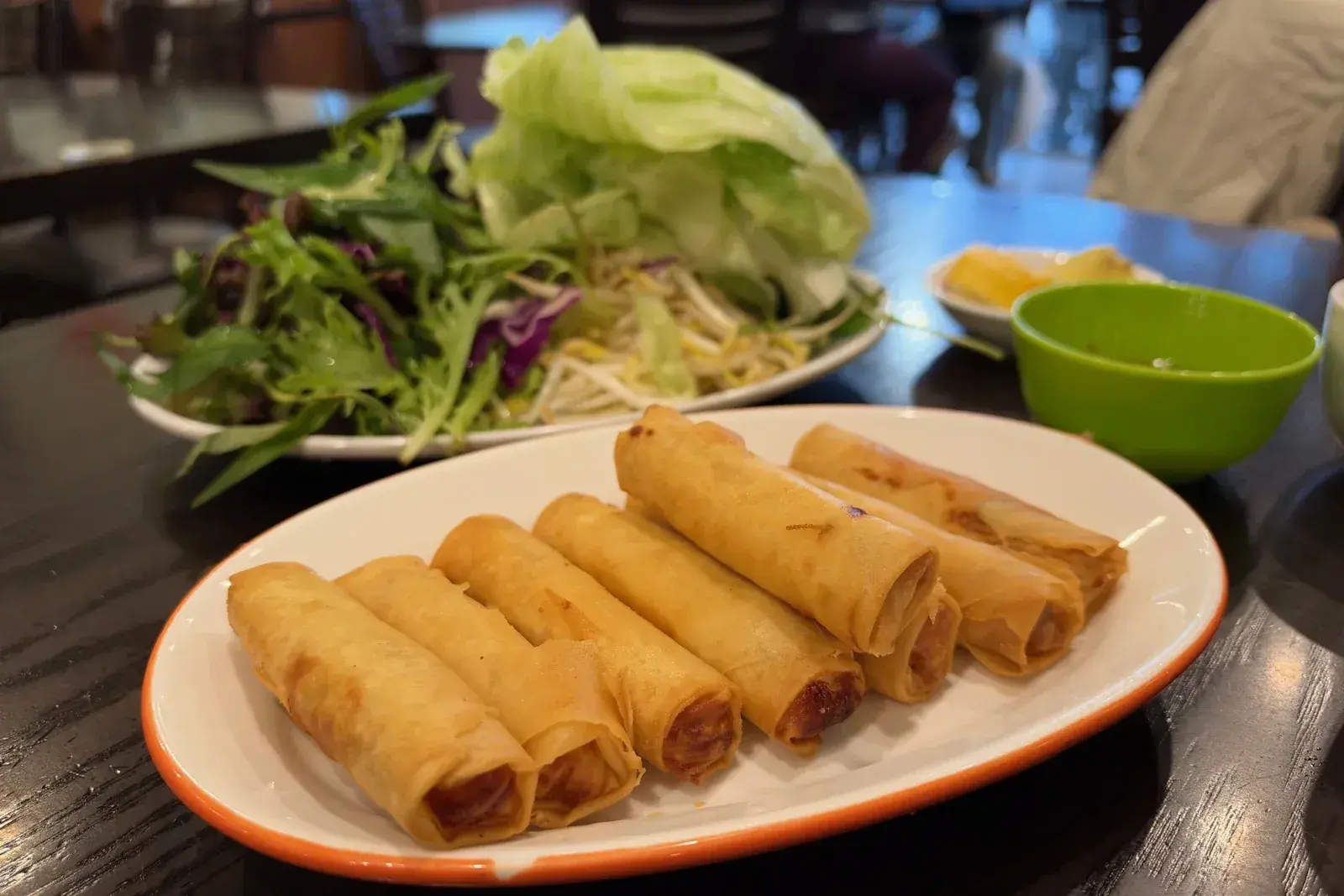 ปอเปี๊ยะทอดเวียดนามวางเรียงบนจาน ด้านหลังเป็นจานผักสดและน้ำจิ้ม